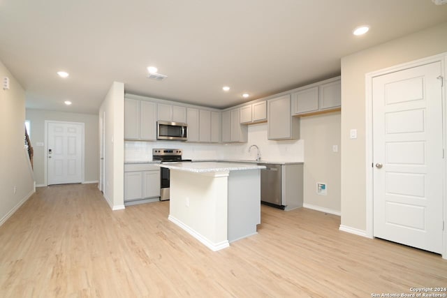 kitchen featuring appliances with stainless steel finishes, a kitchen island, gray cabinetry, sink, and light hardwood / wood-style flooring