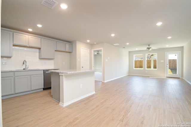 kitchen with sink, tasteful backsplash, gray cabinetry, light stone countertops, and a center island