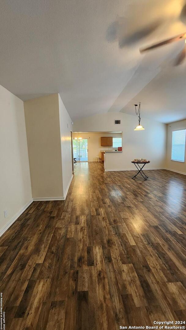 unfurnished living room featuring dark wood-style floors, lofted ceiling, ceiling fan, and baseboards