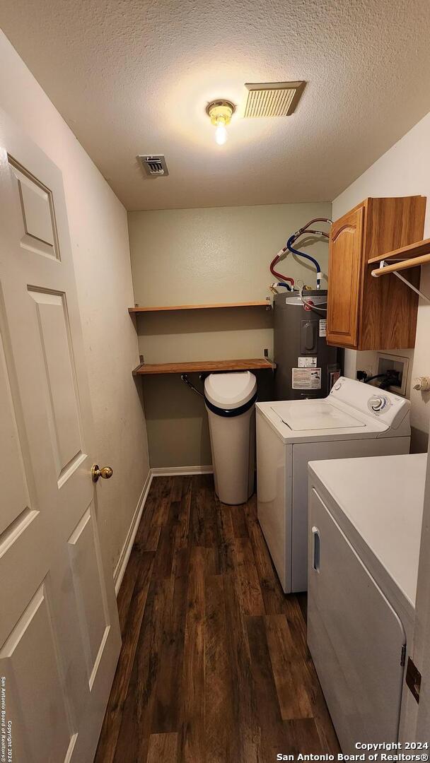 clothes washing area with visible vents, water heater, cabinet space, dark wood-style floors, and washer and clothes dryer