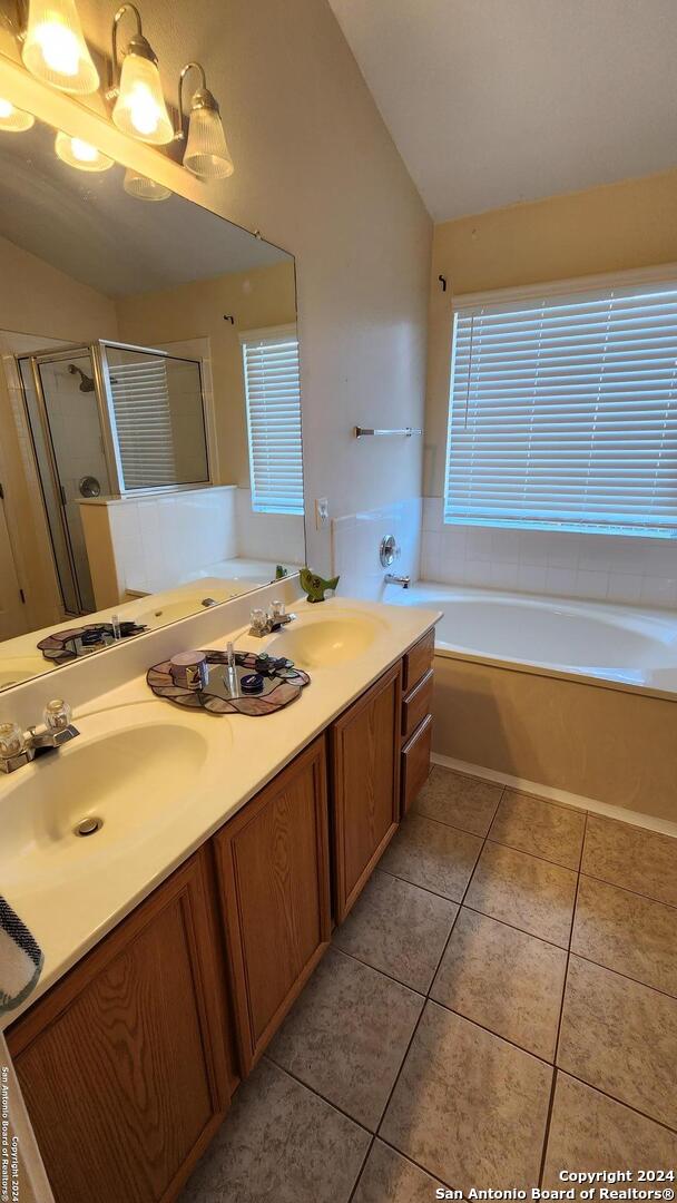 bathroom featuring double vanity, tile patterned floors, a garden tub, a shower stall, and a sink