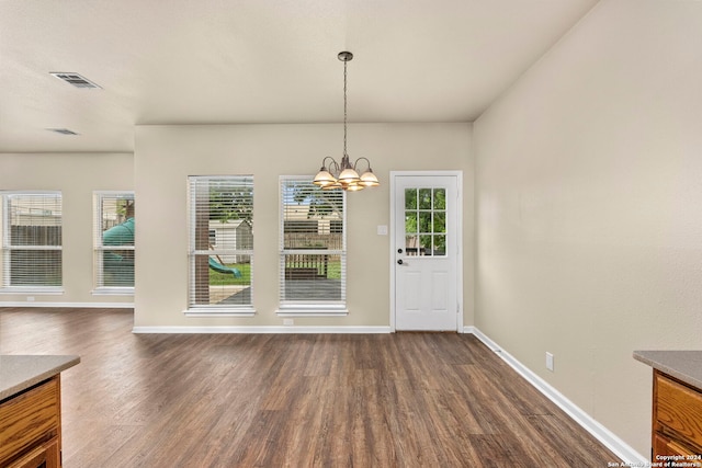 unfurnished dining area with dark wood-type flooring and an inviting chandelier