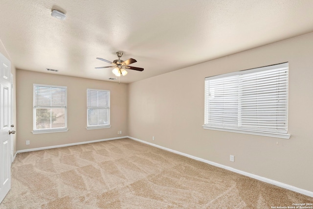 unfurnished room with ceiling fan, a textured ceiling, and light carpet