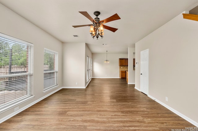 empty room with wood-type flooring and ceiling fan with notable chandelier