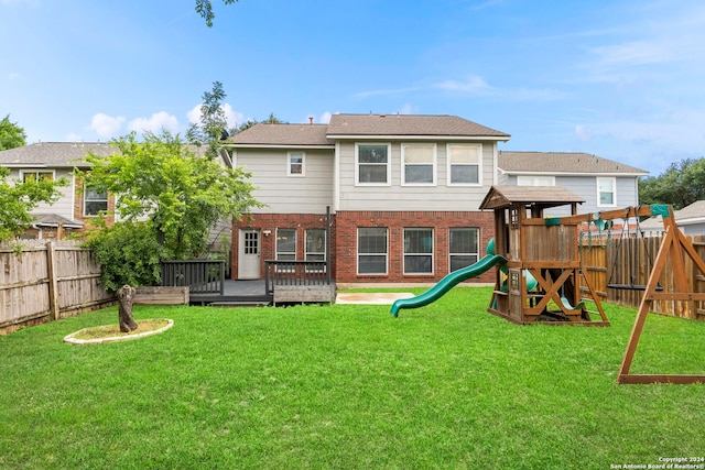 rear view of house featuring a playground, a deck, and a lawn