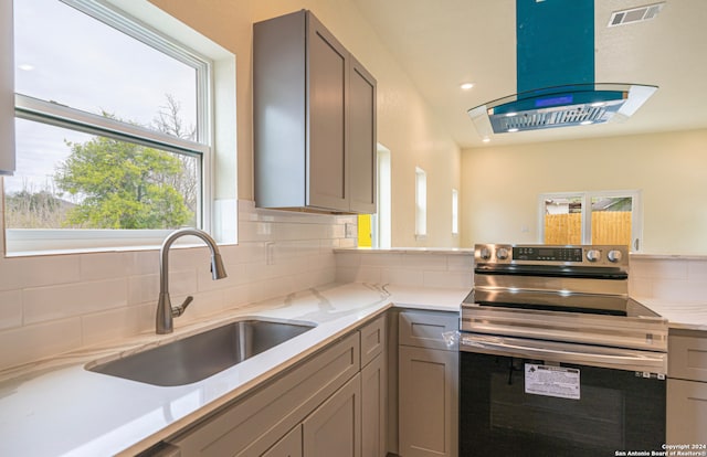 kitchen with sink, gray cabinets, backsplash, island range hood, and stainless steel range with electric cooktop