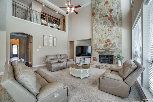 living room featuring crown molding, ceiling fan, a high ceiling, carpet floors, and a stone fireplace