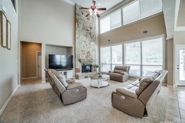 carpeted living room featuring a stone fireplace, ceiling fan, and a high ceiling