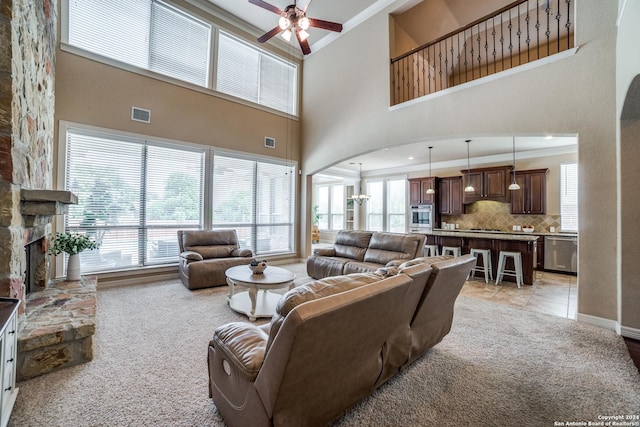 living room featuring a fireplace, a high ceiling, ornamental molding, ceiling fan, and light carpet