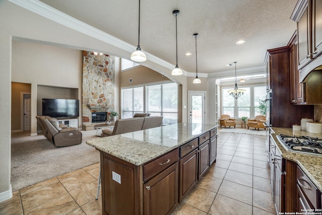 kitchen with hanging light fixtures, light stone countertops, a kitchen island, light carpet, and a stone fireplace