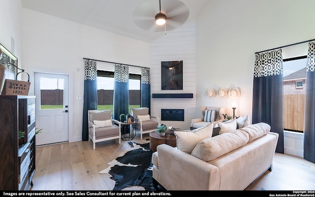 living room with a fireplace, a towering ceiling, light wood-type flooring, and ceiling fan