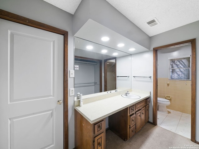 bathroom with tile patterned flooring, tile walls, a textured ceiling, toilet, and vanity