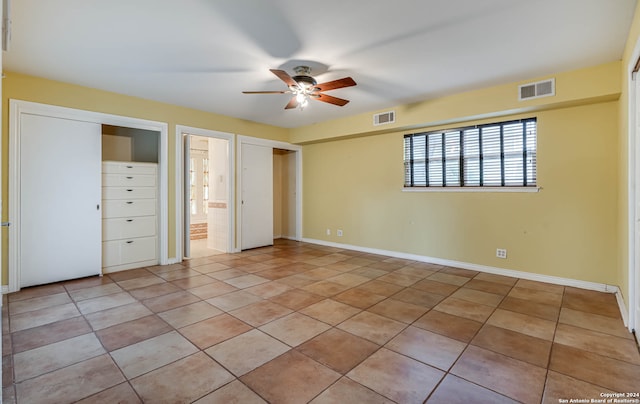 unfurnished bedroom with connected bathroom, light tile patterned floors, and ceiling fan