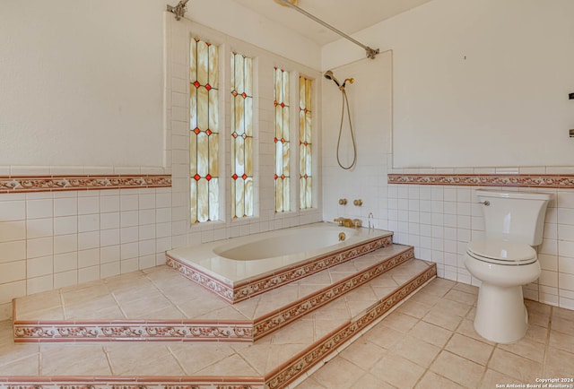 bathroom featuring tile walls, tile patterned floors, toilet, and tiled bath