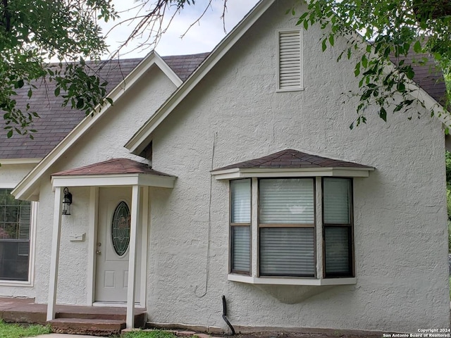 view of exterior entry with roof with shingles and stucco siding