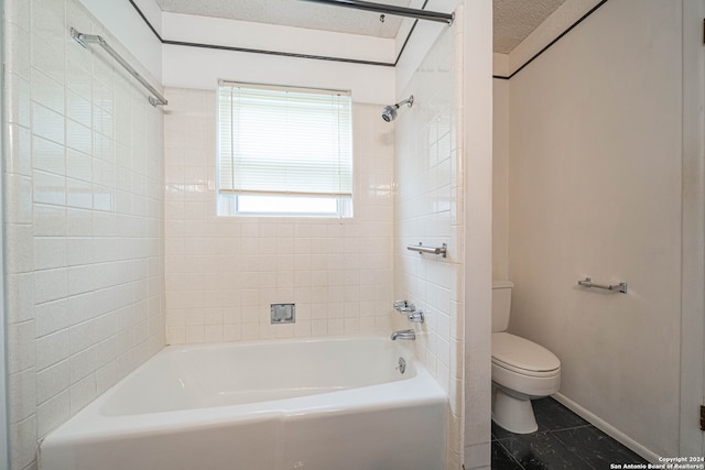 bathroom with tile patterned flooring, tiled shower / bath combo, toilet, and a textured ceiling