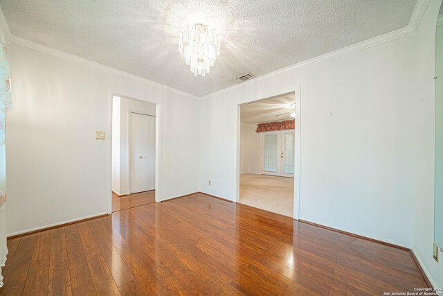 spare room featuring hardwood / wood-style flooring, ceiling fan with notable chandelier, ornamental molding, and a textured ceiling