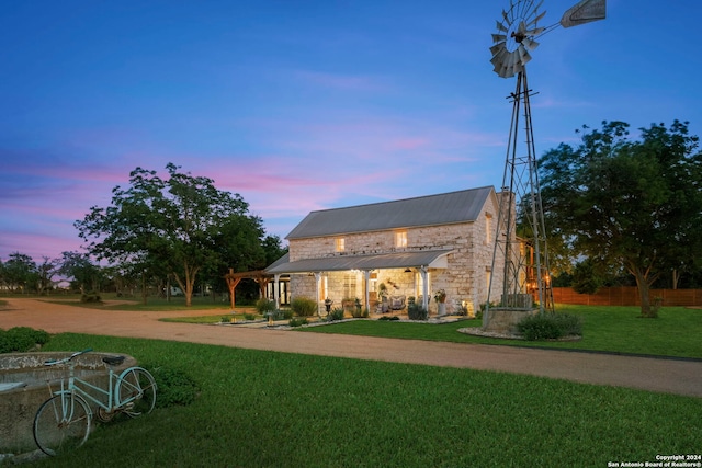 back house at dusk with a pergola and a lawn