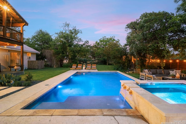 pool at dusk featuring an in ground hot tub, pool water feature, a yard, and an outdoor hangout area