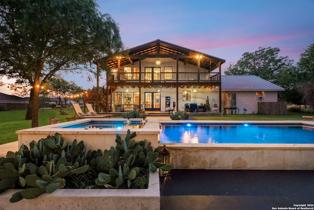 pool at dusk with a patio area, an in ground hot tub, and a lawn