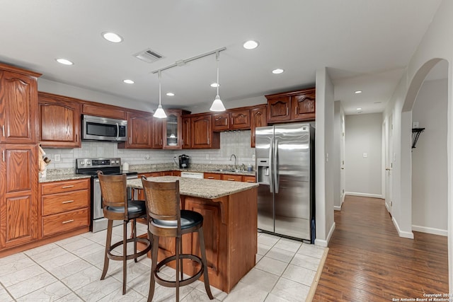 kitchen with sink, light stone counters, a kitchen island, stainless steel appliances, and decorative backsplash