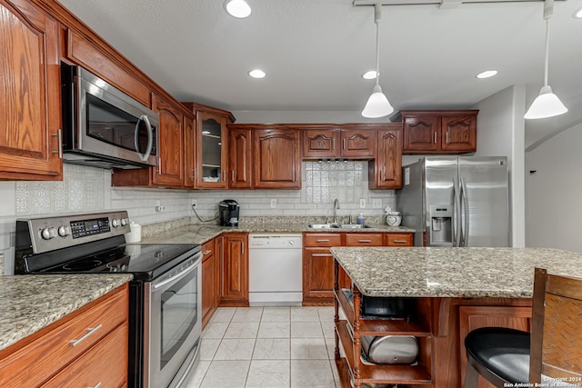 kitchen with a breakfast bar, sink, hanging light fixtures, light stone counters, and stainless steel appliances