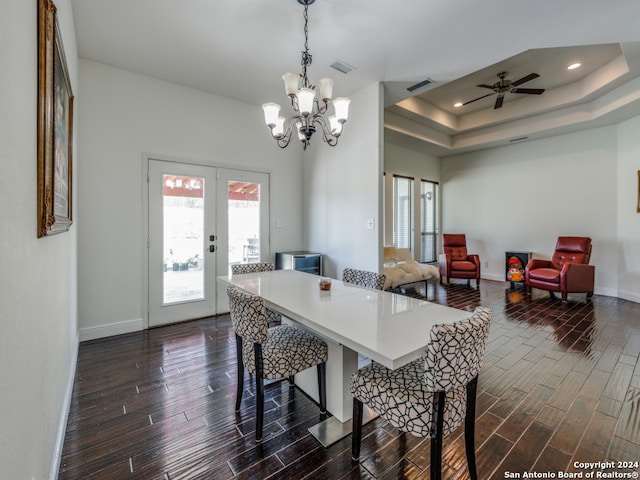 dining space featuring dark wood-type flooring, ceiling fan with notable chandelier, a raised ceiling, and french doors