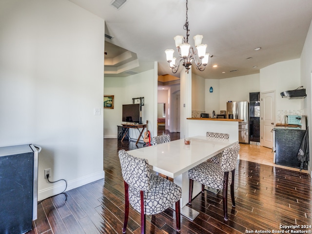 dining space with a tray ceiling, wood-type flooring, and an inviting chandelier