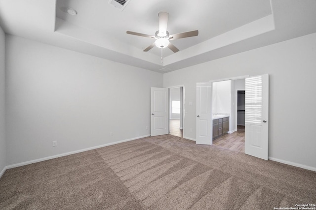 unfurnished bedroom with light carpet, ensuite bath, a raised ceiling, and ceiling fan