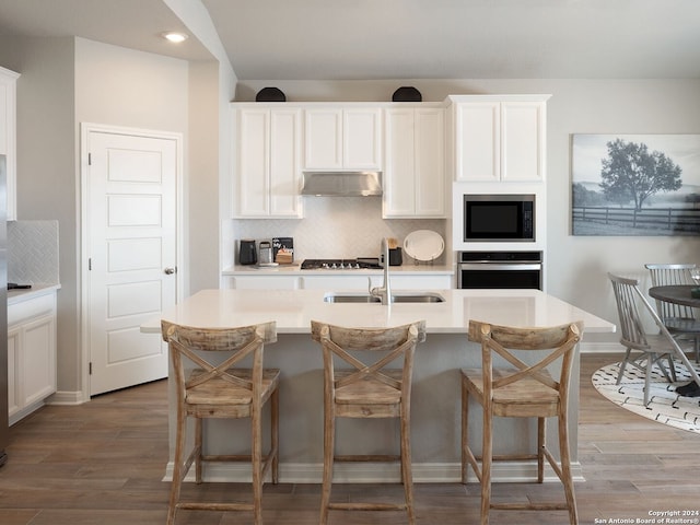 kitchen with hardwood / wood-style flooring, white cabinetry, appliances with stainless steel finishes, and a kitchen breakfast bar