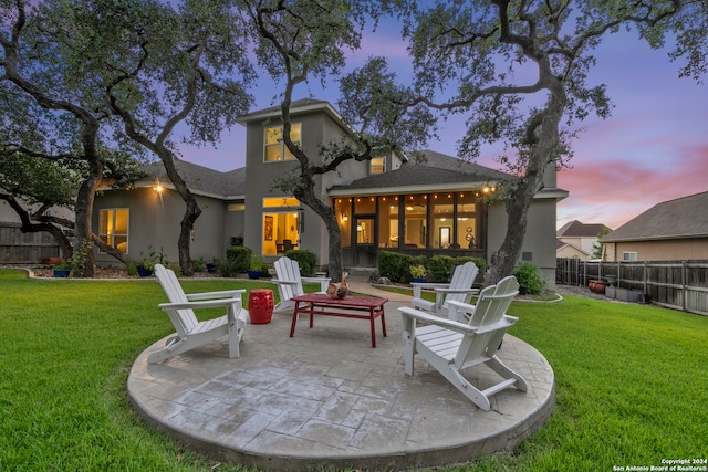 back house at dusk featuring a patio area and a lawn