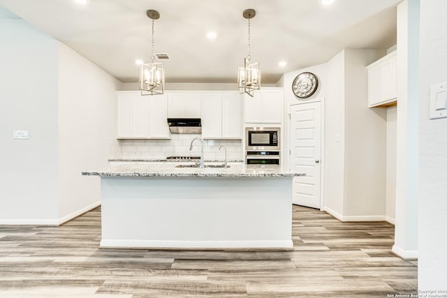 kitchen with a kitchen island with sink, black microwave, tasteful backsplash, white cabinets, and stainless steel oven