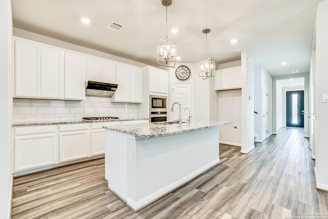 kitchen featuring appliances with stainless steel finishes, white cabinetry, hanging light fixtures, light stone countertops, and a center island with sink