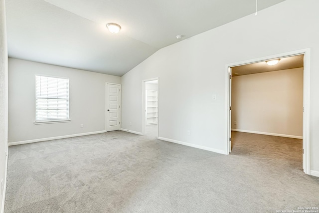 unfurnished bedroom with light carpet, a walk in closet, a closet, and vaulted ceiling