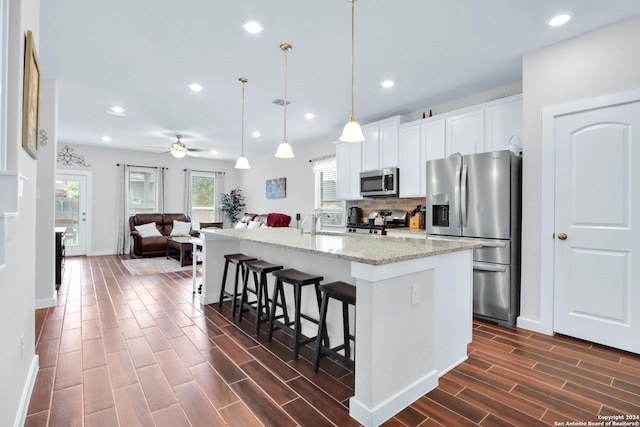 kitchen with a breakfast bar, white cabinetry, an island with sink, pendant lighting, and stainless steel appliances