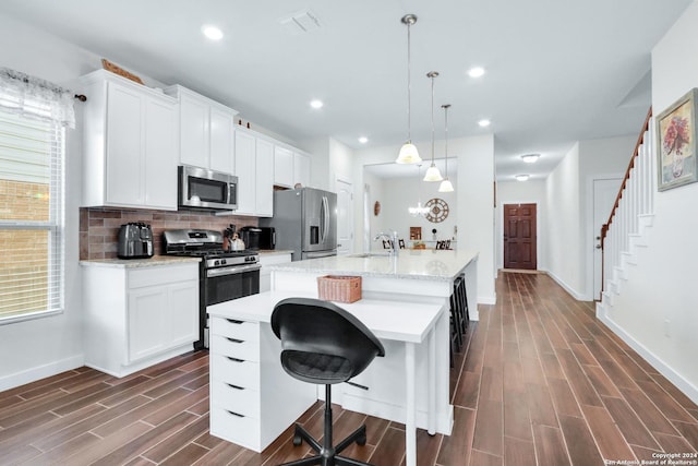 kitchen with hanging light fixtures, appliances with stainless steel finishes, a kitchen breakfast bar, decorative backsplash, and white cabinets