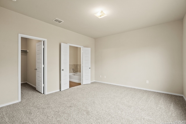 unfurnished bedroom with carpet floors, ensuite bath, a spacious closet, and a closet