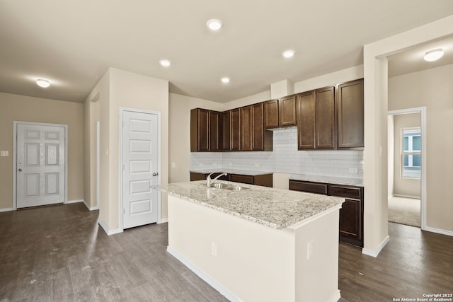 kitchen with a center island with sink, hardwood / wood-style floors, sink, light stone counters, and backsplash