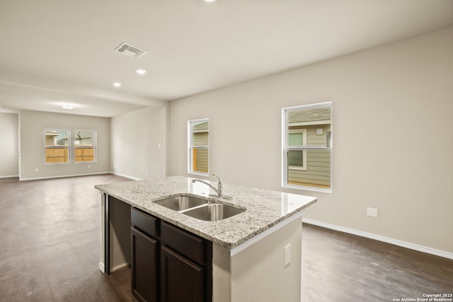 kitchen with sink, light stone countertops, dark hardwood / wood-style floors, dark brown cabinetry, and a kitchen island with sink