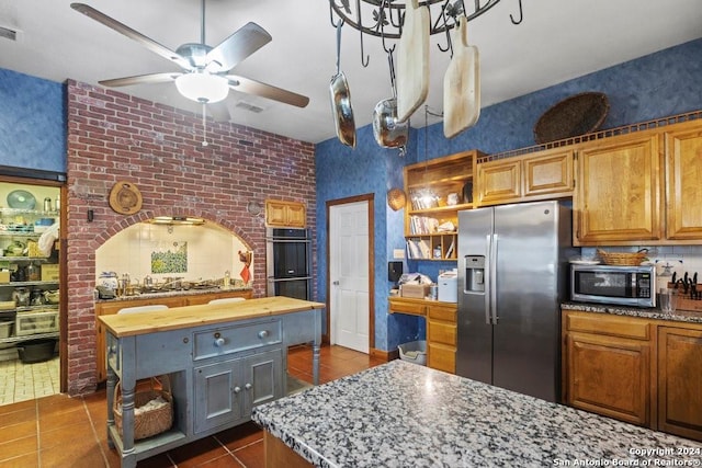 kitchen with butcher block countertops, dark tile patterned floors, stainless steel appliances, a center island, and brick wall