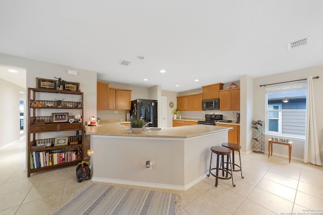 kitchen with light tile patterned flooring, black appliances, and a kitchen bar