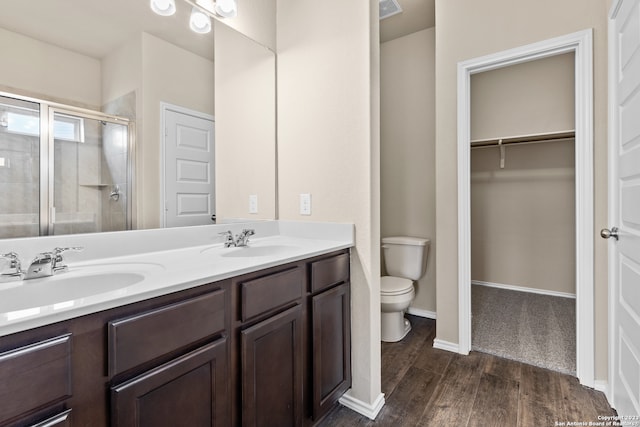 bathroom featuring a shower with shower door, double vanity, hardwood / wood-style flooring, and toilet