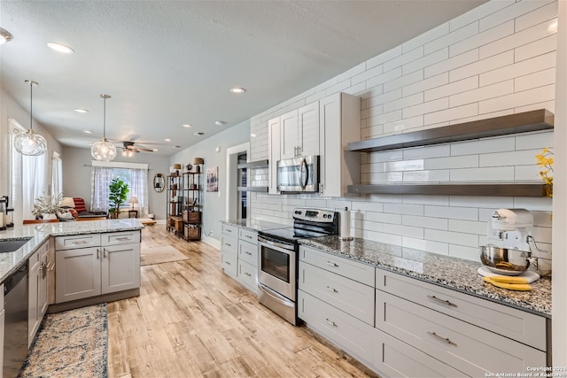 kitchen with stainless steel appliances, pendant lighting, light stone counters, light hardwood / wood-style floors, and decorative backsplash