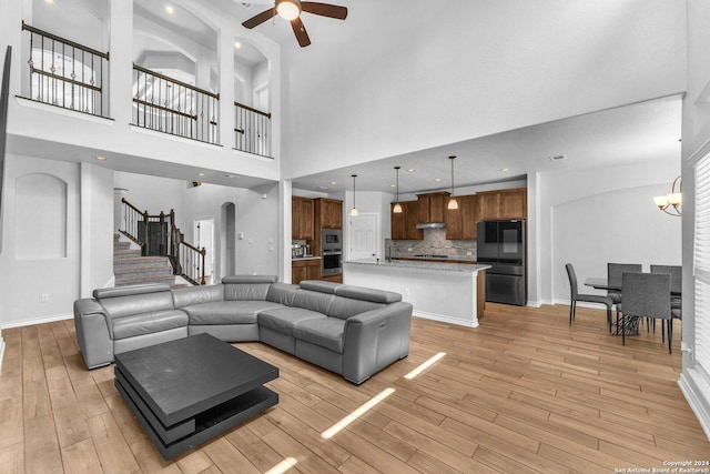 living room with a high ceiling, ceiling fan with notable chandelier, and light hardwood / wood-style floors