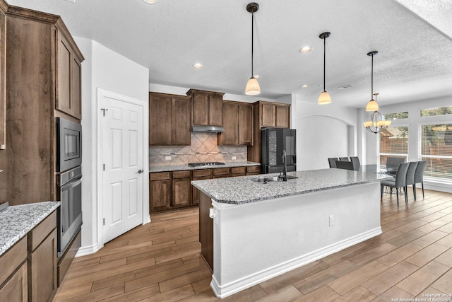 kitchen featuring sink, tasteful backsplash, hanging light fixtures, appliances with stainless steel finishes, and an island with sink