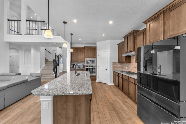 kitchen featuring sink, appliances with stainless steel finishes, a spacious island, tasteful backsplash, and decorative light fixtures