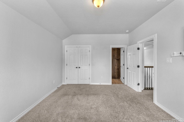 unfurnished bedroom featuring vaulted ceiling, light carpet, a textured ceiling, and a closet