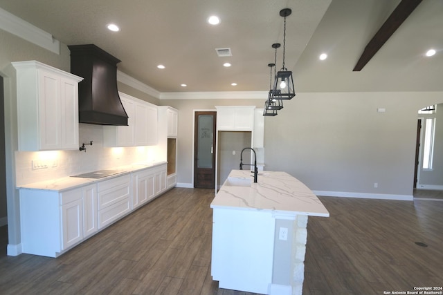 kitchen featuring a kitchen island with sink, decorative light fixtures, custom range hood, and white cabinets