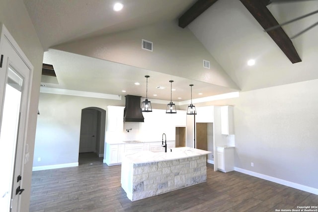 kitchen featuring custom exhaust hood, hanging light fixtures, light stone countertops, a kitchen island with sink, and white cabinets