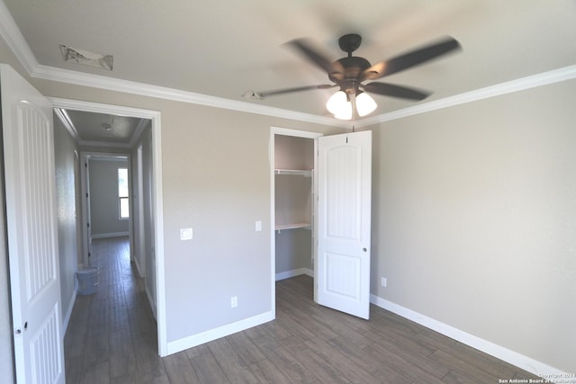 unfurnished bedroom featuring ceiling fan, dark hardwood / wood-style floors, ornamental molding, a walk in closet, and a closet